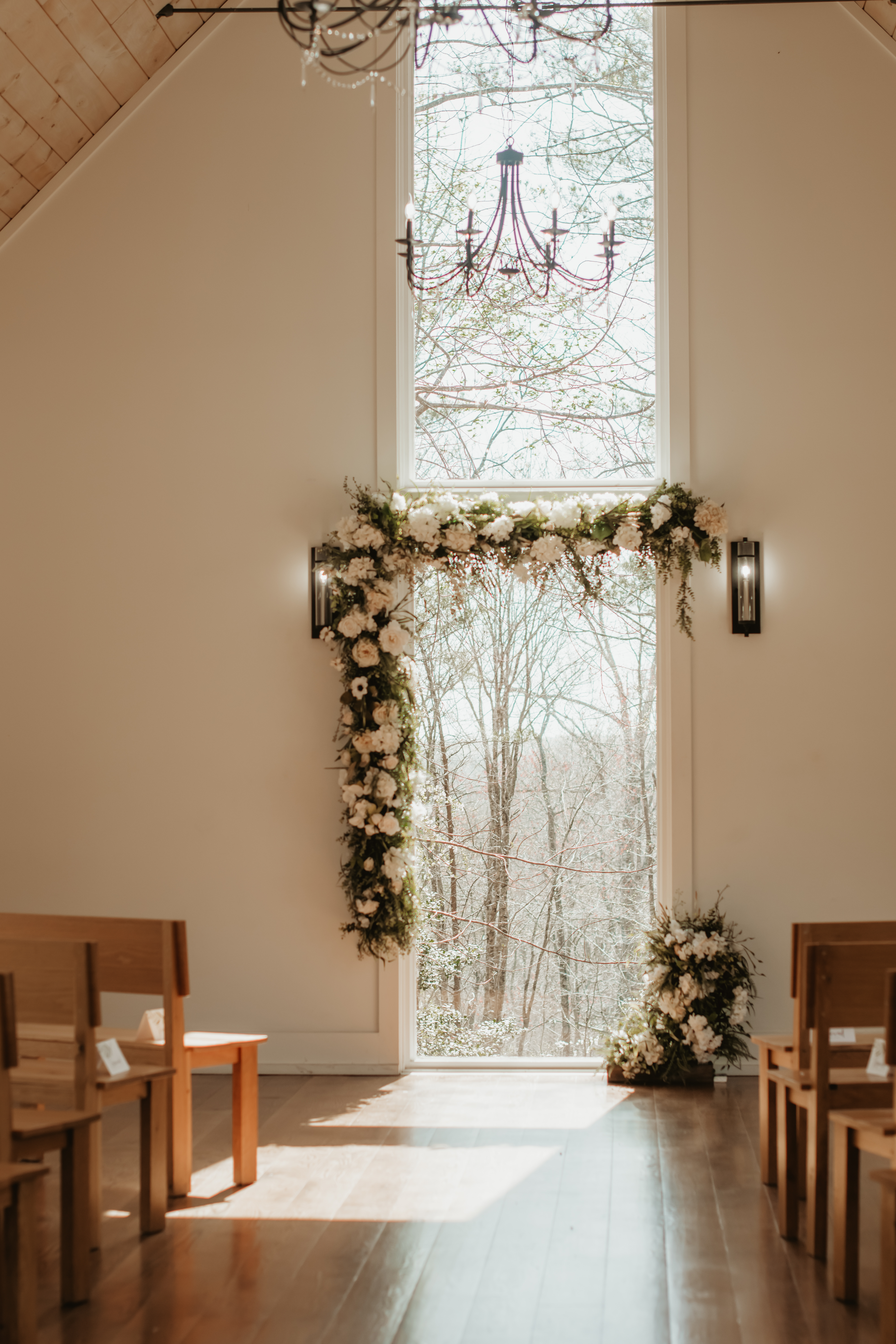 a photo of a wedding altar decorated with a flower arch, the sun is coming in through the window