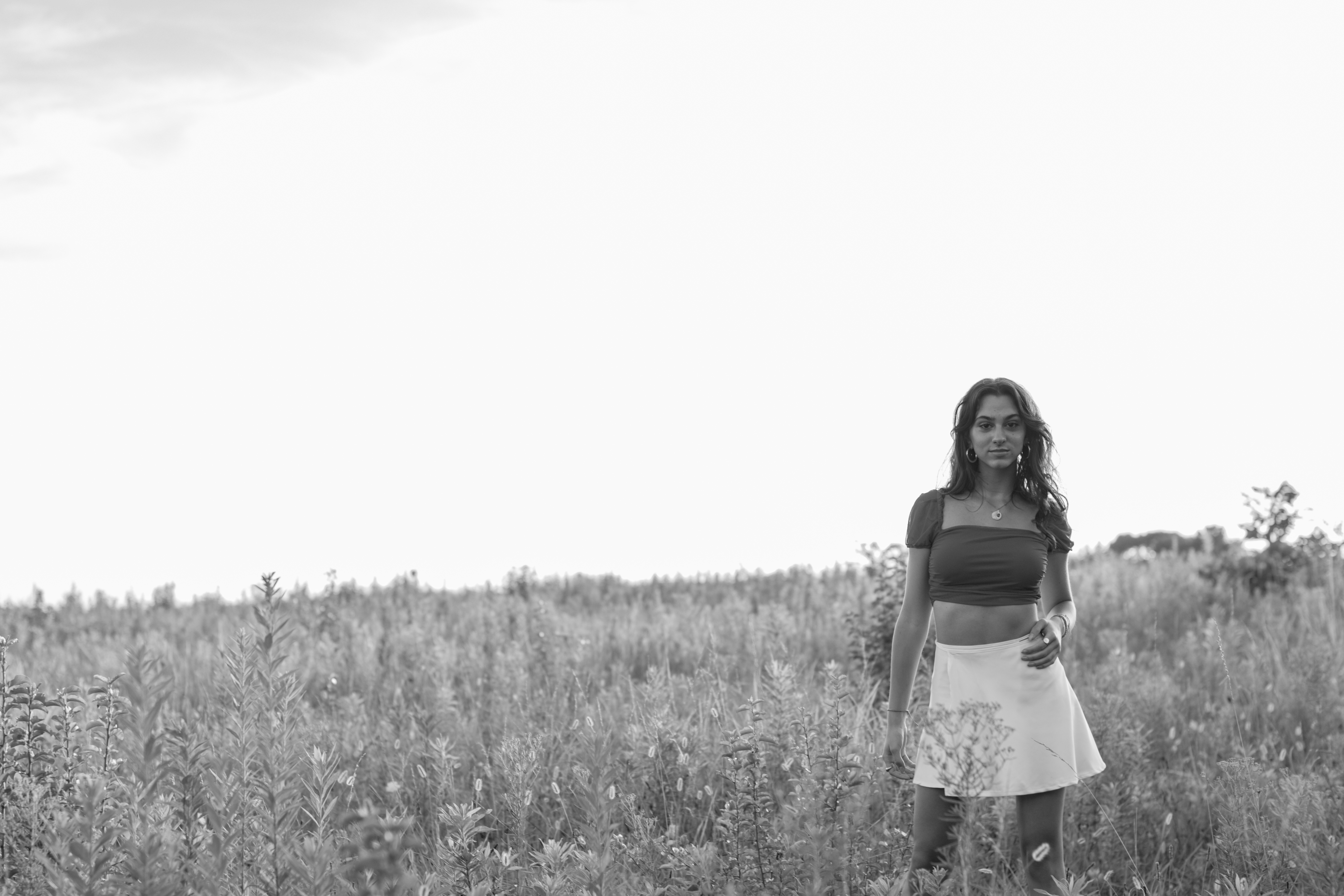 a black and white image of a girl standing in a feild, she is on the right side of the photo, the rest is white space sky