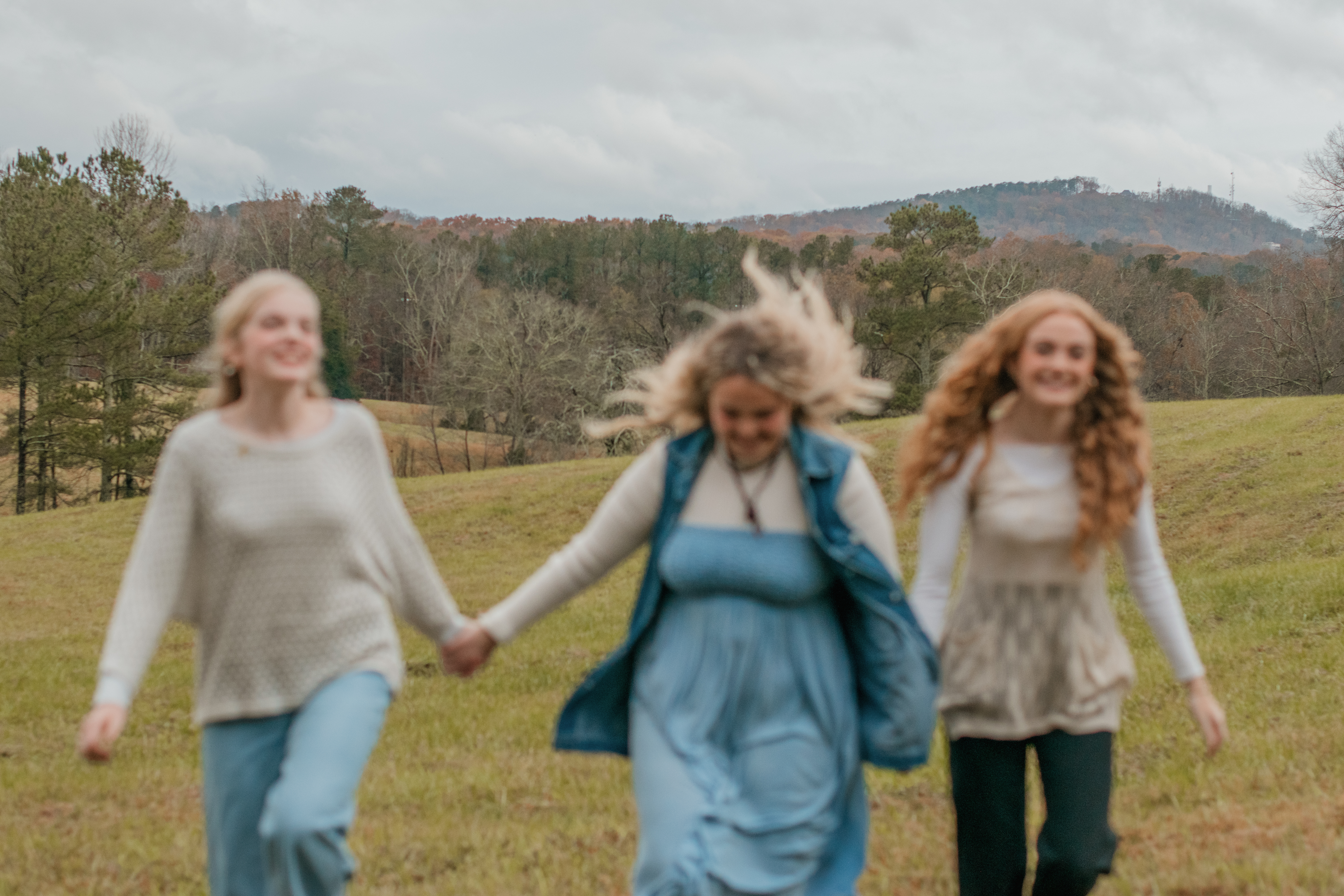 an out-of-focus photo of three girls running through a feild with a mountain in the background