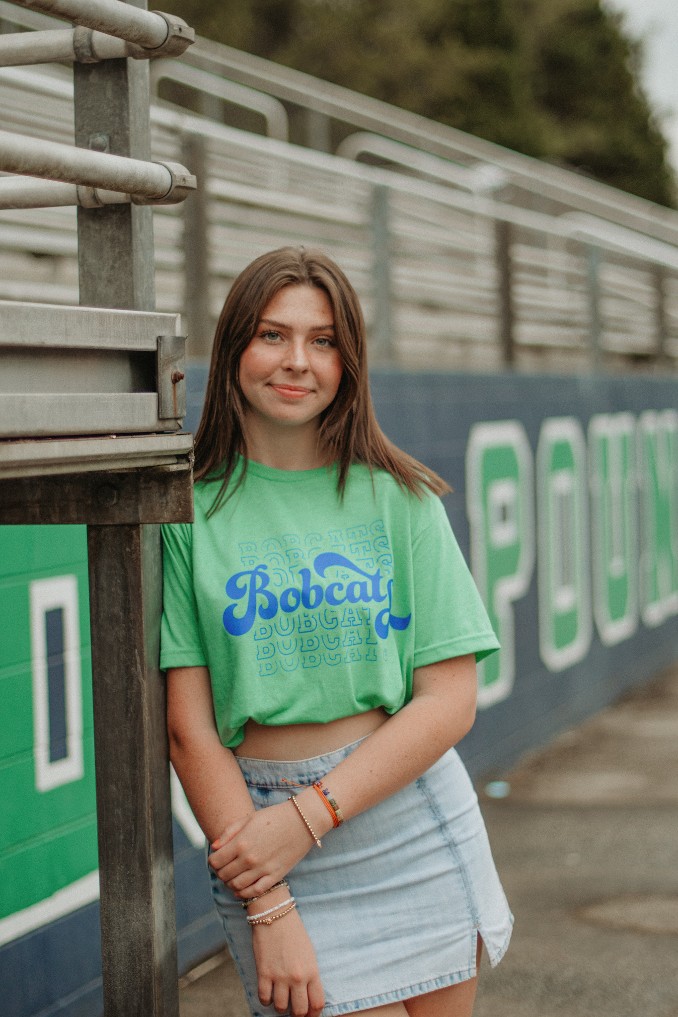 a girl in a college t-shirt leaning against her high school's bleachers