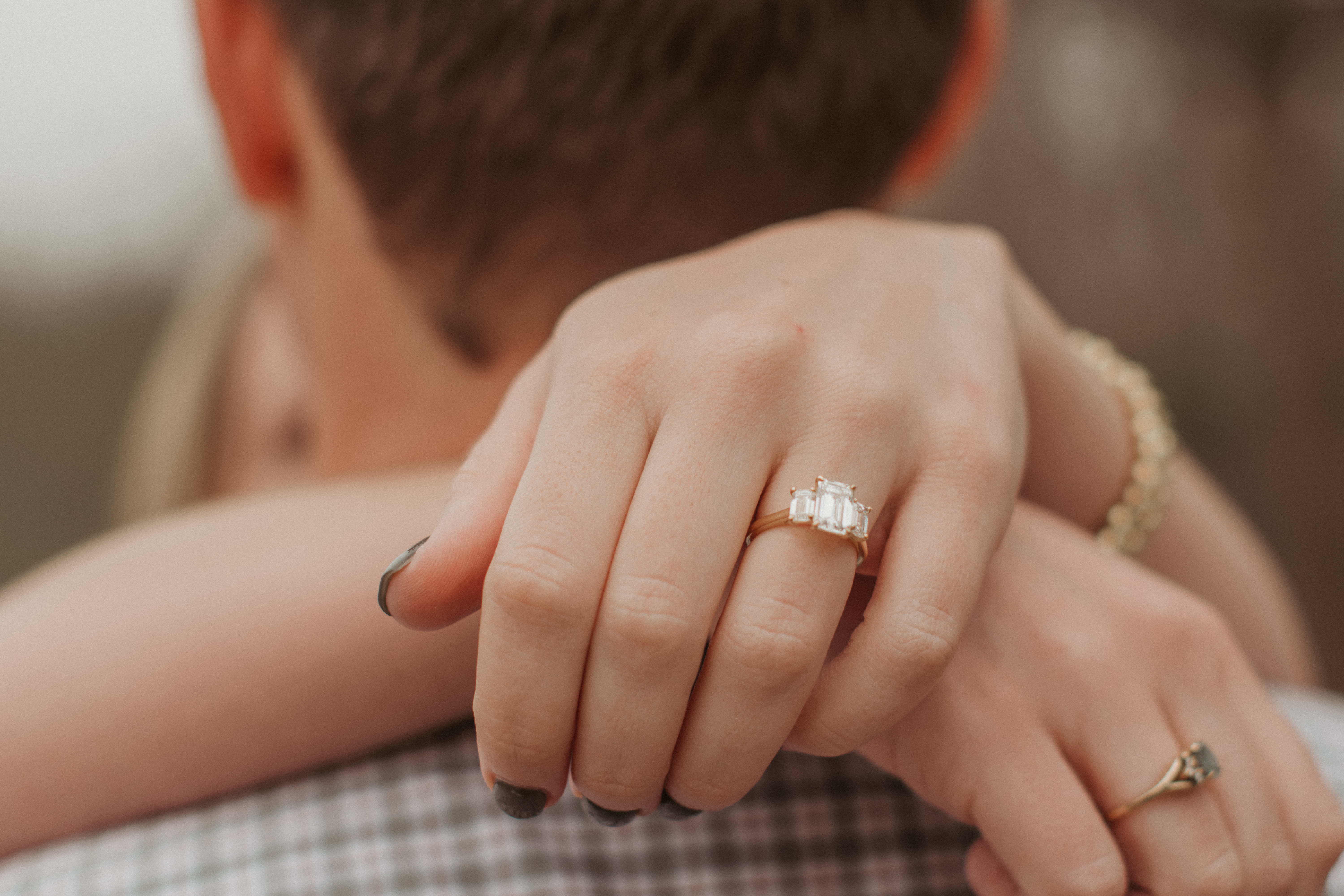 a close-up shot of an engagement ring on the hand of the girl that is wrapped behind the guy's neck